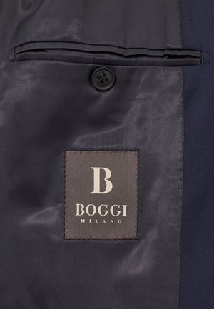 Sinih suit material dengan tekstur halus, menampilkan saku kiri dan kancing gelap. Termasuk label kain abu-abu dengan "BOGGI MILANO" dalam warna putih.