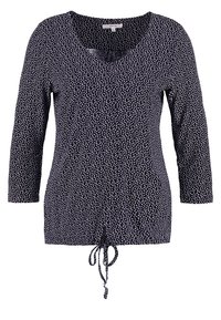 Námořnický top s výstřihem do V a rukávy tříčtvrtě. Obsahuje bílý abstraktní vzor a šňůrku na lemu pro nastavitelnou velikost.