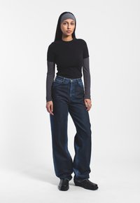 Camiseta negra ajustada sobre una camiseta de manga larga gris, combinada con jeans de pierna ancha de tiro alto en azul oscuro y botines negros.