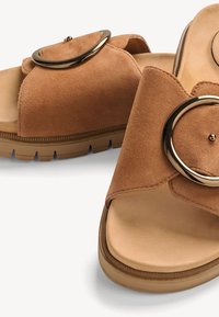 Braune Wildleder-Sandalen mit offenem Zehenbereich, großer goldener runder Schnalle und dicker, profillierter Gummisohle.