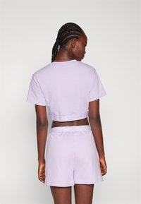 Ensemble de t-shirt court et de shorts couleur lilas en tissu doux. Présente une bande avec logo au niveau de la taille et une coupe décontractée. Texture lisse dans l'ensemble.