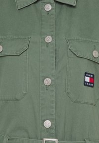 Khakigrünes Hemd mit silbernen Druckknöpfen, zwei Brusttaschen und einem mehrfarbigen Tommy Jeans Logo-Patch auf der linken Tasche.