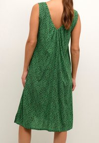 Vestido sin mangas verde con un escote en V, que presenta un patrón de estampado de leopardo, textura suave y una silueta fluida que llega hasta la mitad de la pantorrilla.