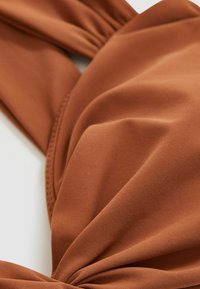 Brunt texturerat tyg med vriden design, som har ett mjukt och elastiskt material. Närbilden framhäver veck och en knuten detalj.