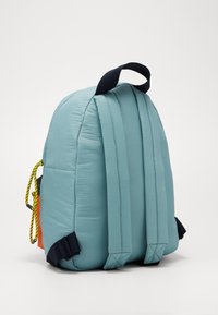 Zaino imbottito blu chiaro con manico nero, spallacci regolabili e dettaglio del cordoncino giallo su sfondo bianco.