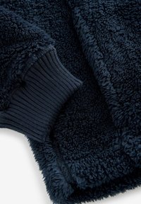 Couverture en polaire bleu marine avec une surface douce et texturée, des poignets côtelés et un design confortable. Idéale pour la chaleur et le confort.