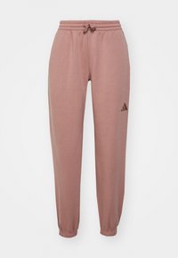 Pantaloni jogger rosa realizzati in tessuto morbido, con vita elasticizzata e cordino, e polsini affusolati. Dettaglio del logo nero sul lato.