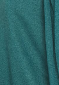 Tela de algodón verde azulado, textura suave, mostrando pliegues y caídas, con un sutil brillo. No hay patrones ni herrajes visibles.