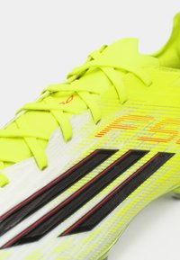 Κίτρινα ποδοσφαιρικά παπούτσια με μαύρες και κόκκινες λεπτομέρειες, διαθέτοντας υφή, ελαφριά επάνω επιφάνεια και διακριτό σχέδιο με τρεις ρίγες.