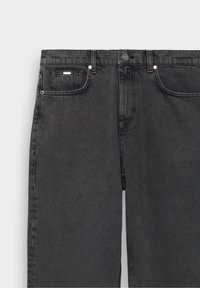 Jean en denim noir à coupe droite. Comprend cinq poches, fermeture par bouton métallique et détails de couture subtils. Texture douce, taille mi-haute.