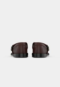 Sandales en cuir brun avec une semelle noire plate, dotées d'un détail de boucle de chaque côté et d'un design à dos ouvert. Texture lisse dans l'ensemble.