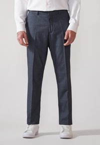 Pantaloni a quadri blu scuro, con una texture liscia e dettagli delle pieghe, abbinati a sneakers bianche. Vestibilità su misura con passanti per cintura.