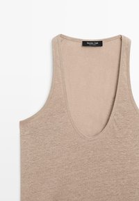 Beige sleeveless tank top with deep scoop neckline, made of soft knit fabric, featuring a small black brand label at inner back collar.