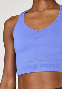 Μωβ αθλητικό σουτιέν Nike Pro με σχεδιασμό V-neck, κατασκευασμένο από λείο ύφασμα. Διαθέτει διακριτικό λογότυπο και σήμανση στη λαστιχένια ταινία.