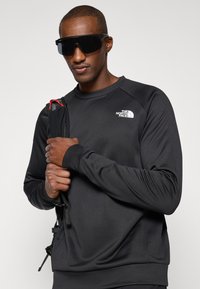Čierna mikina s dlhým rukávom s okrúhlym výstrihom a raglánovými rukávmi. Na prednej strane sa nachádza logo The North Face. Hladká, ľahká látka.
