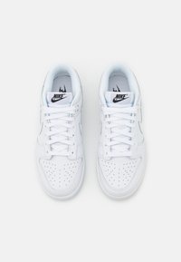 Baskets en cuir blanc avec des détails perforés, des lacets plats et un logo noir sur la languette, présentant un design bas et un col rembourré.