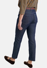 Tamne traperice tamne boje s ravnim krojem, s leđnim džepovima i blago suženi nastavci. Uparene s pletenim remenom i smeškim baletankama.