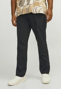 Pantalones de algodón negros con un corte relajado, con bolsillos laterales y una textura suave, combinados con zapatillas blancas.