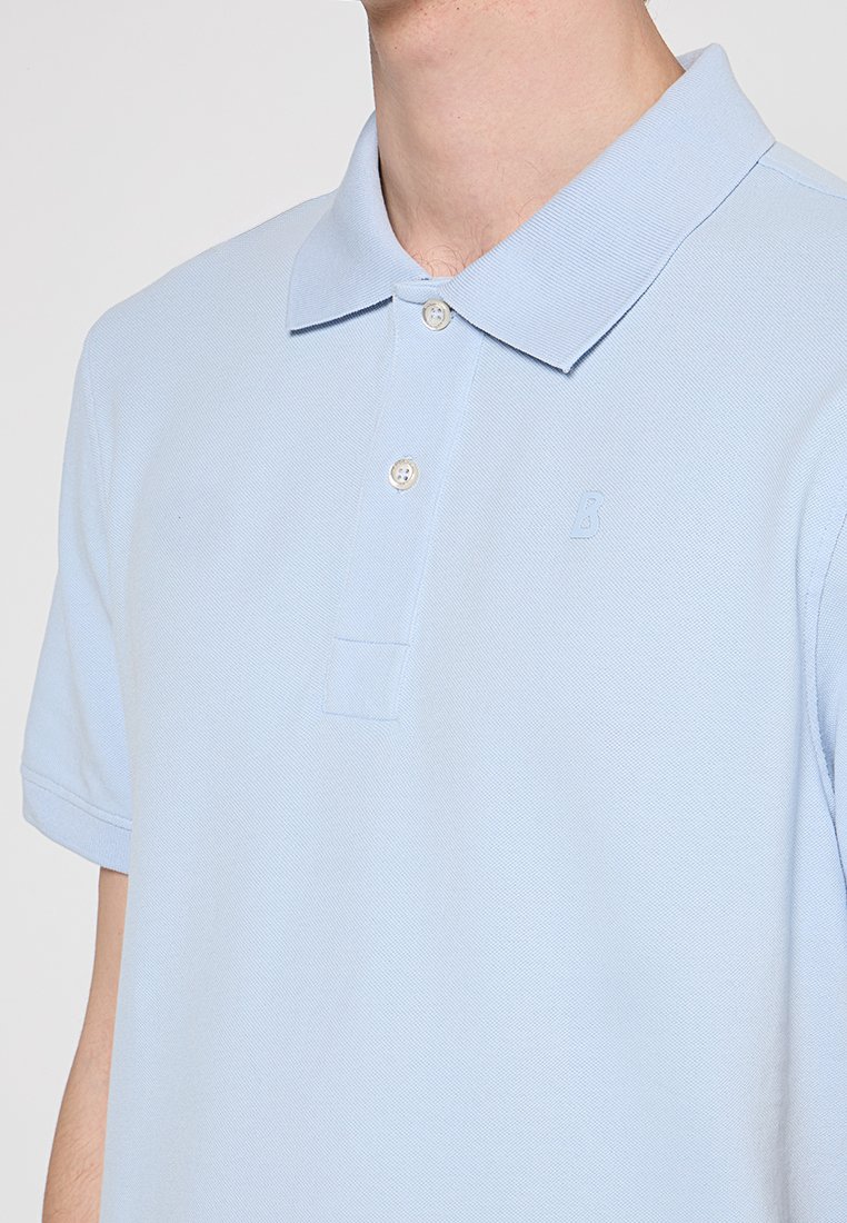 Hellblaues Polohemd aus strukturiertem Stoff, mit klassischem Kragen, zwei Knöpfen und einem kleinen, auf der Brust gestickten Logo.