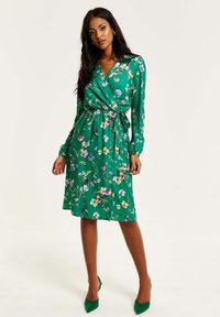 Floral green wrap dress with long sleeves and a tie waist. Features vibrant multi-colored floral patterns and a soft, smooth texture.