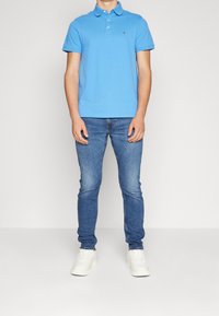 Modrá polo tričko se třemi knoflíky, spárované se světle modrými džíny a bílými teniskami. Slim fit design, hladká textura a neformální styl.