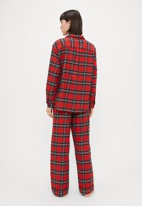 Rødternet pyjamas sæt med en knap-op skjorte med krave og løstsiddende bukser. Stoffet ser blødt ud med et ternet mønster.