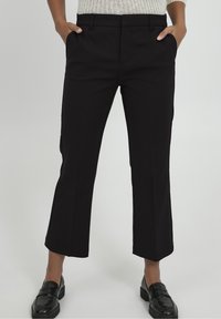 Schwarze, taillierte Cropped-Hosen aus glattem Stoff mit seitlichen Taschen. Sie verfügen über einen flachen Bund und Gürtelschlaufen. Kombiniert mit schwarzen Loafers.