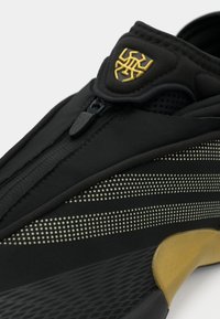 Czarny but sportowy z zamkiem błyskawicznym, ozdobiony kropkowaną teksturą i złotym detalem na pięcie. Elegancki design z elastycznego materiału.