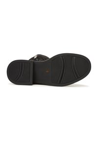 Suela de bota de goma negra con una superficie texturizada y líneas curvas. Presenta un logo central y tacones distintivos para mayor agarre.