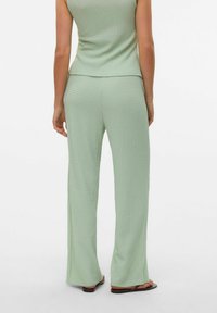 Ljust grön texturerad topp och byxor med avslappnad passform, med texturerad yta och slitsar på byxbenen. Minimal detaljering.