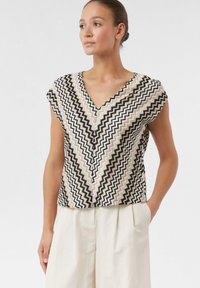 V-hals top met korte mouwen met een zigzagpatroon in beige, zwart en wit. Gemaakt van lichtgewicht stof met een relaxte pasvorm.