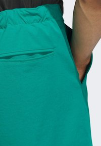 Close-up van groene stof met een zachte textuur, een elastische tailleband aan de bovenkant en een klein zakje aan de rechterkant.