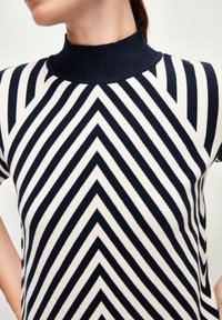 Hnědo-námořnický pruhovaný pletený top s vysokým žebrovaným límcem a vzorem ve tvaru šípu, který se vyznačuje přiléhavým střihem a hladkou strukturou.