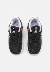 Zapatillas negras con parte superior de tela texturizada, suela blanca y cordones negros. Presenta la marca de Hello Kitty en la lengüeta y detalles rojos.