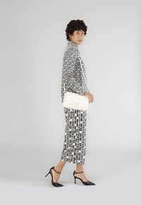 Sorte og hvide mønstrede tøj med en løs bluse og cropped bukser, parret med en hvid tekstureret håndtaske og sorte spidse hæle.