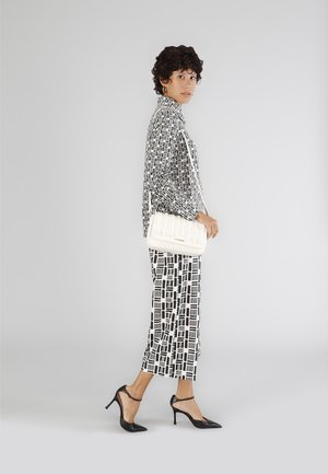 Sorte og hvide mønstrede tøj med en løs bluse og cropped bukser, parret med en hvid tekstureret håndtaske og sorte spidse hæle.