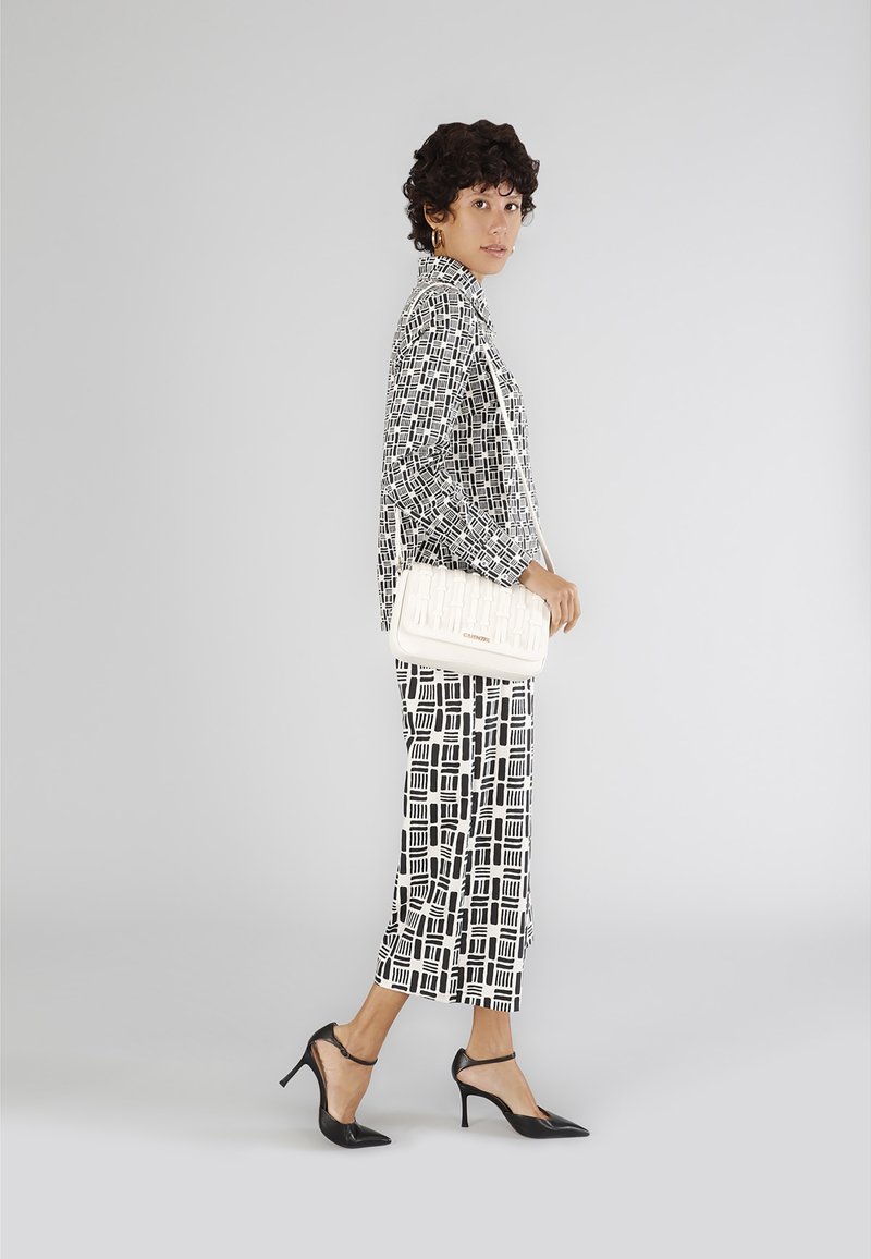 Sorte og hvide mønstrede tøj med en løs bluse og cropped bukser, parret med en hvid tekstureret håndtaske og sorte spidse hæle.