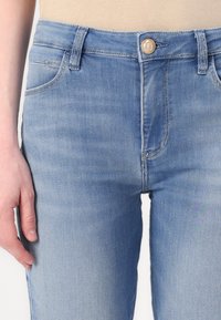 Light blue denim jeans with a fitted design, front pockets, button closure, and visible stitching details. Smooth texture, mid-rise waist.