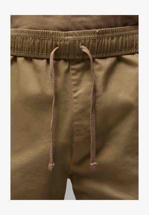 Brązowe bawełniane szorty z elastycznym paskiem w talii i sznurkiem. Zawierają kieszeń boczną, gładką fakturę i luźny krój.