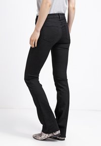 Black denim flared jeans with a mid-rise waist and back pockets. The fabric is smooth with a slight stretch, paired with patterned boots.