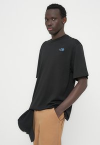 Μαύρο βαμβακερό t-shirt με στρογγυλή λαιμόκοψη και κοντά μανίκια. Διαθέτει ένα μικρό μπλε λογότυπο στο αριστερό στήθος. Κανονική εφαρμογή.