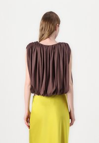 Brown draped blouse with a gathered neckline, paired with a smooth, bright yellow skirt. The fabric is lightweight with a soft texture.