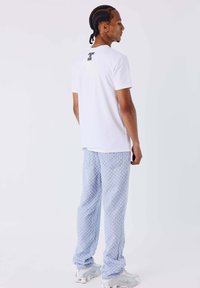 Camiseta blanca de manga corta con la frase "CHANGE THE GAME" impresa en la espalda, combinada con pantalones azul claro con estampado y zapatillas grises.