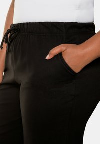 Schwarze Jogginghose aus weichem Stoff mit elastischem Bund, Kordelzug und seitlichen Taschen für zusätzlichen Komfort.