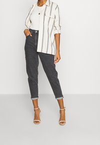 Lätt krämfärgad skjorta med knappar och svarta vertikala ränder över en vit linne, parat med mörk denim som är uppvikt vid anklarna och naken strappy klackar.