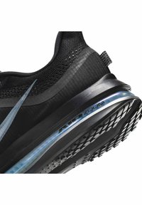 Gros plan d'une basket noire Nike Air Zoom montrant une tige texturée, une semelle intermédiaire translucide bleue avec coussin d'air et une semelle extérieure en caoutchouc à motifs.
