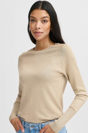 Maglione beige a maniche lunghe in un tessuto a maglia liscia con scollatura rotonda e polsini a coste, abbinato a jeans di denim blu chiaro.