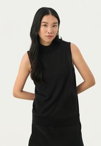 Mustat ilmanhihoja turtleneck-toppi, joka on valmistettu pehmeästä materiaalista, siinä on tiukka malli ja ribsireunus, yhdistettynä mustiin hameeseen.
