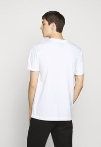 White cotton t-shirt with short sleeves and a crew neckline. Displayed from the back, featuring a relaxed fit and minimal branding.
