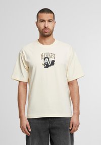 Cremefarvet bomulds T-shirt med afslappet pasform, der har et grafisk print af en skunk-figur og ordet "MARKET" i dekorativ skrift.